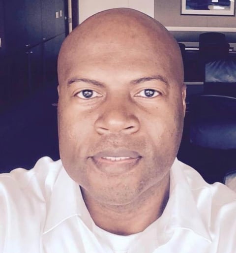 Portrait of a bald man with a warm smile wearing a white t-shirt, taken indoors